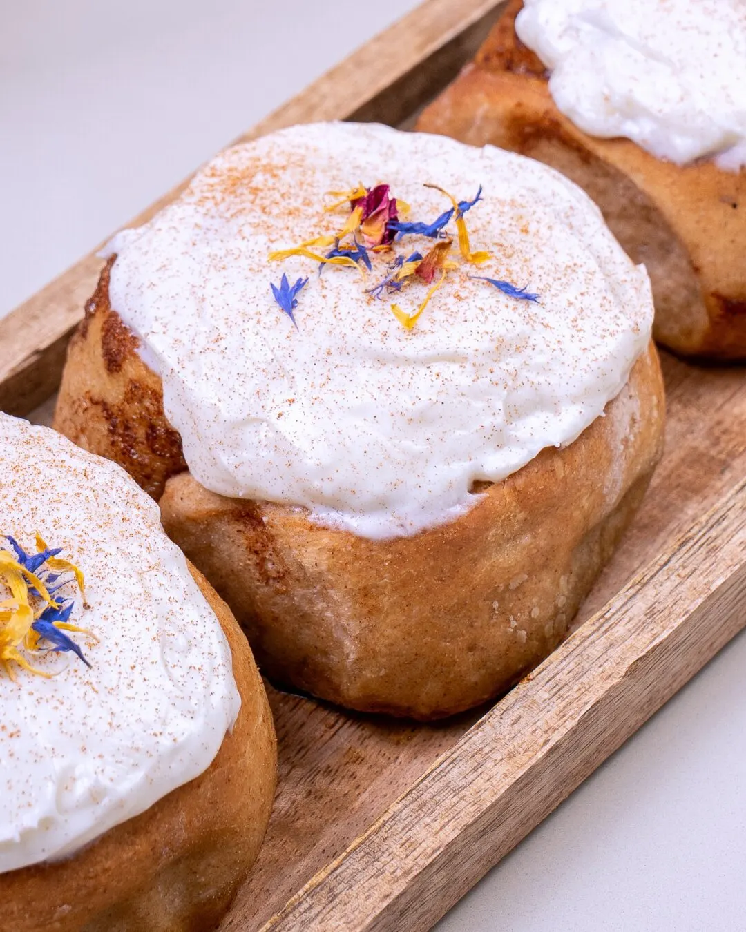 Rollos de canela glaseados con flores comestibles sobre una bandeja de madera.
