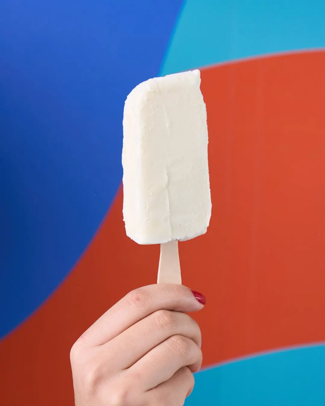 Mano sosteniendo una paleta blanca frente a un fondo rojo y azul.